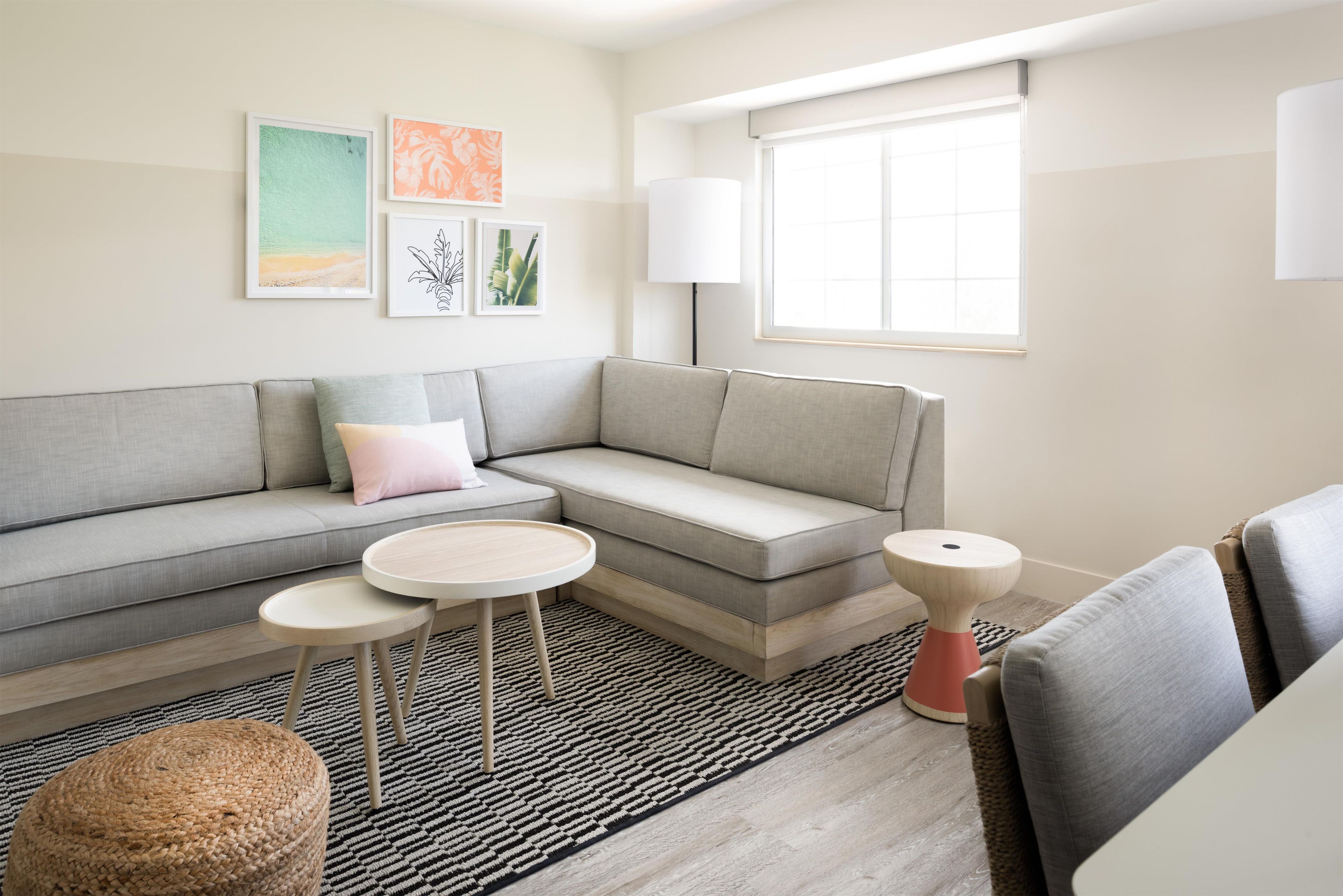 A modern living room with a grey sofa, a round coffee table, a small side table, a lamp, and a window with blinds.
