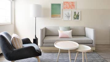 A modern living room with a grey sofa, a black and white patterned rug, a round wooden coffee table, and a floor lamp.