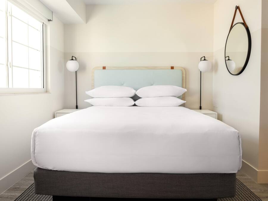 A neatly made bed with white linens, a light blue headboard, and two bedside lamps.