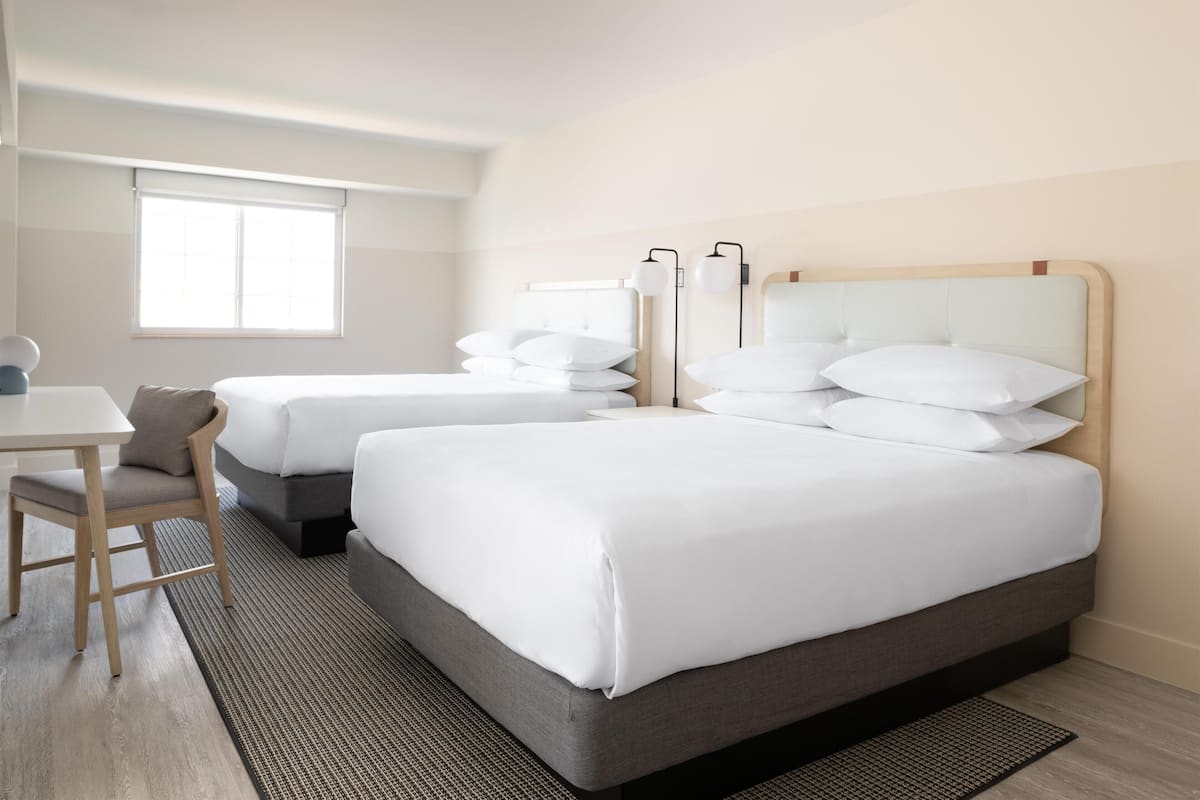 A hotel room with two beds, a desk, and a window.