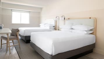Quarto de hotel com duas camas, uma escrivaninha e uma janela.