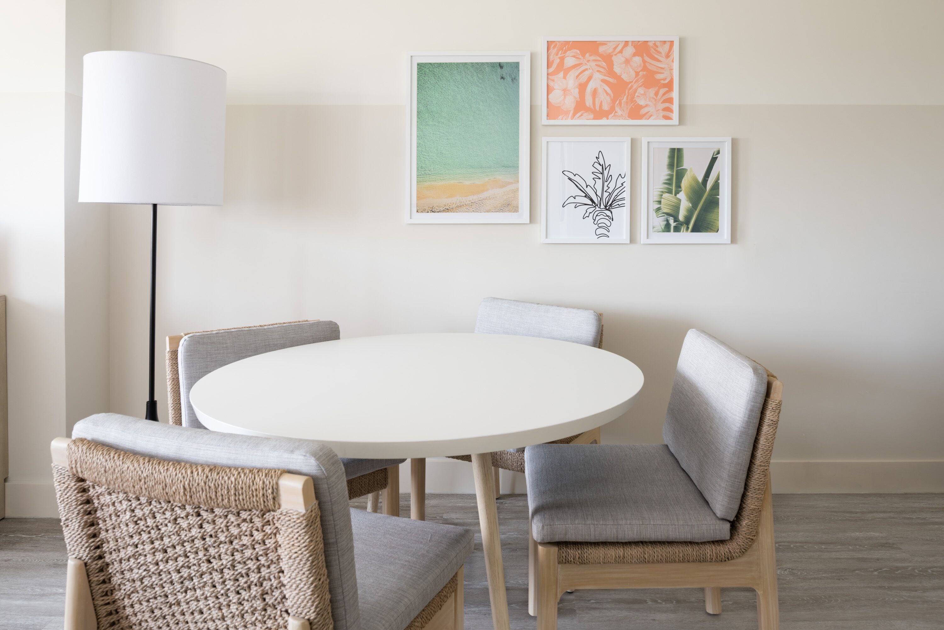 A round dining table with four chairs, a floor lamp, and three framed artworks on the wall.