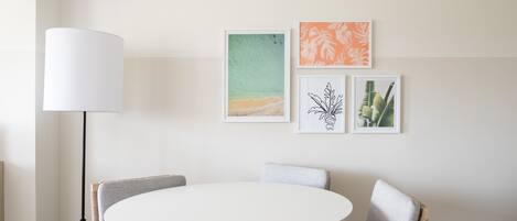 A round dining table with four chairs, a floor lamp, and three framed artworks on the wall.