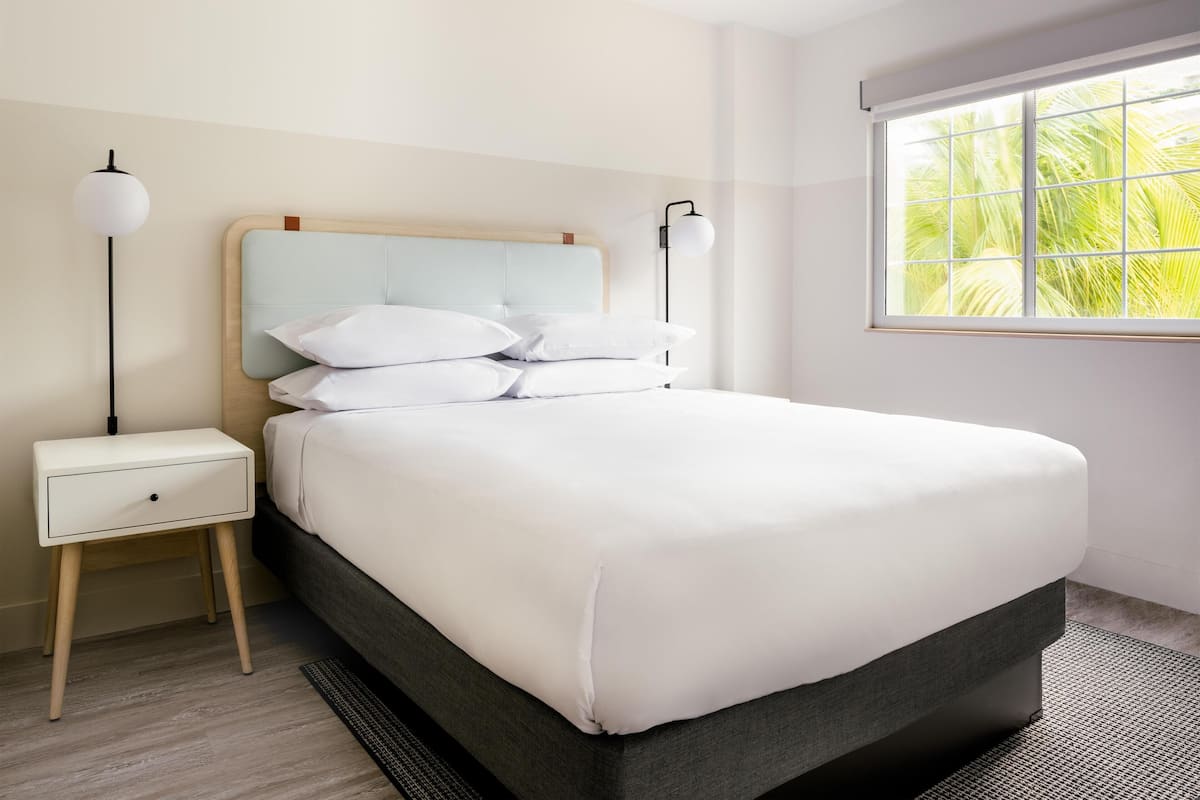A neatly made bed with white bedding, a wooden headboard, and two bedside lamps.