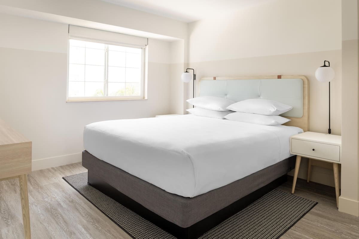 A modern bedroom with a large bed, bedside tables, a window, and a nightstand.