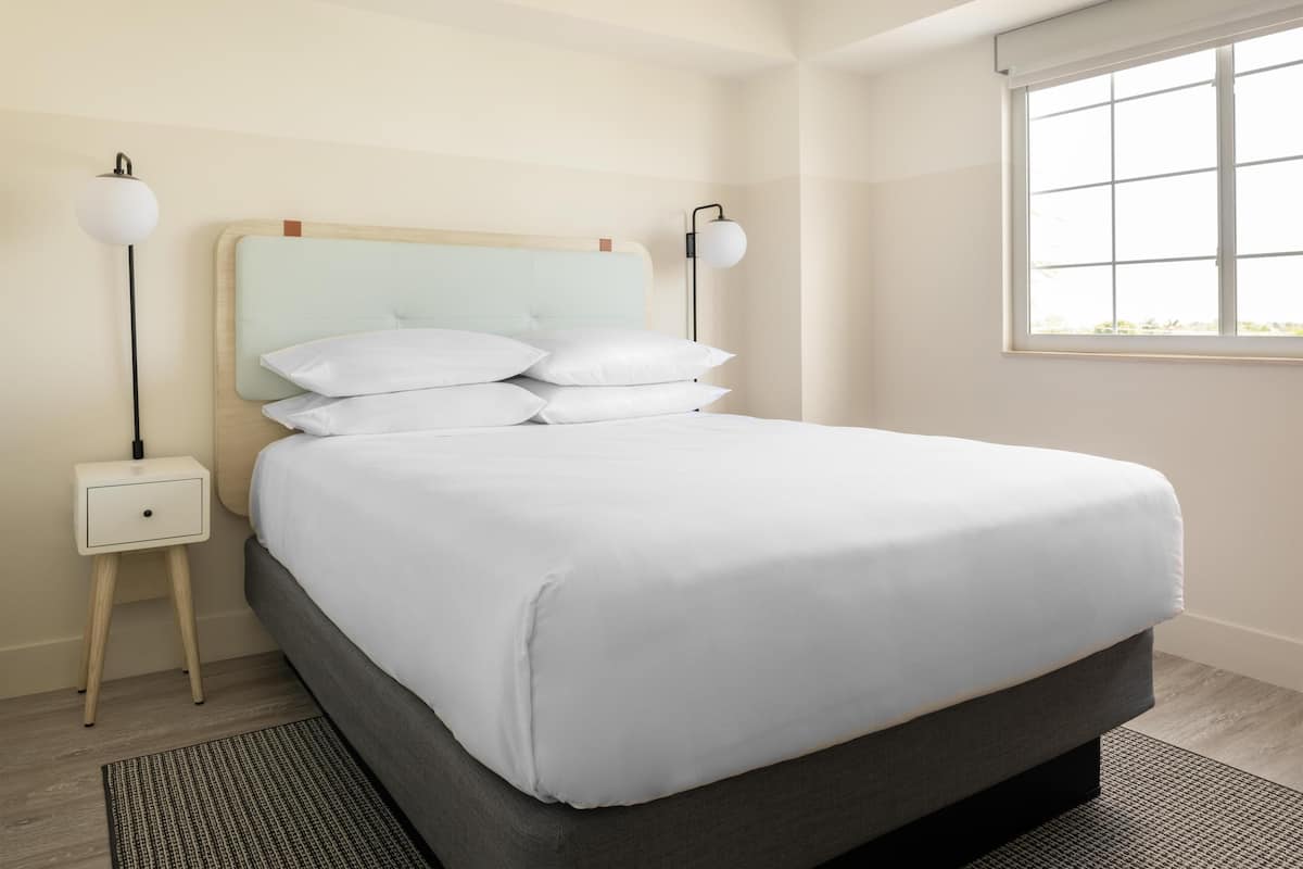 A neatly made bed with white linens, a wooden headboard, and two bedside lamps.