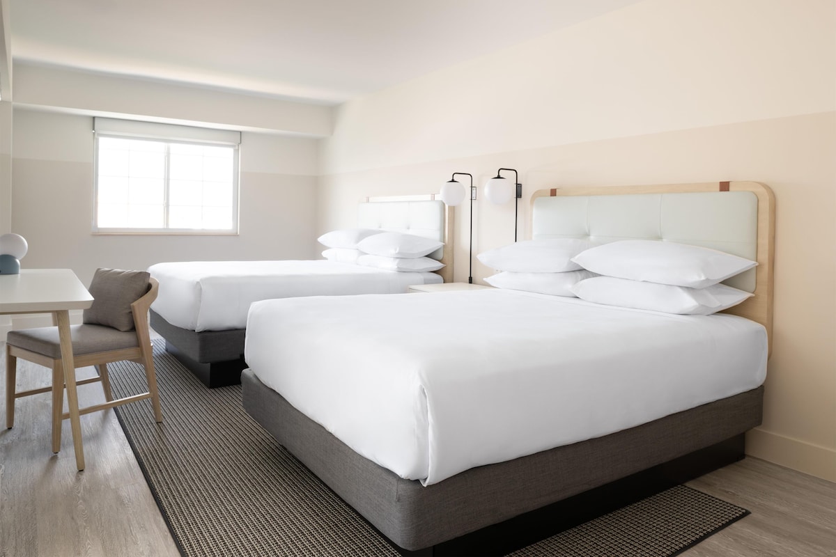 A hotel room with two beds, a desk, and a window.