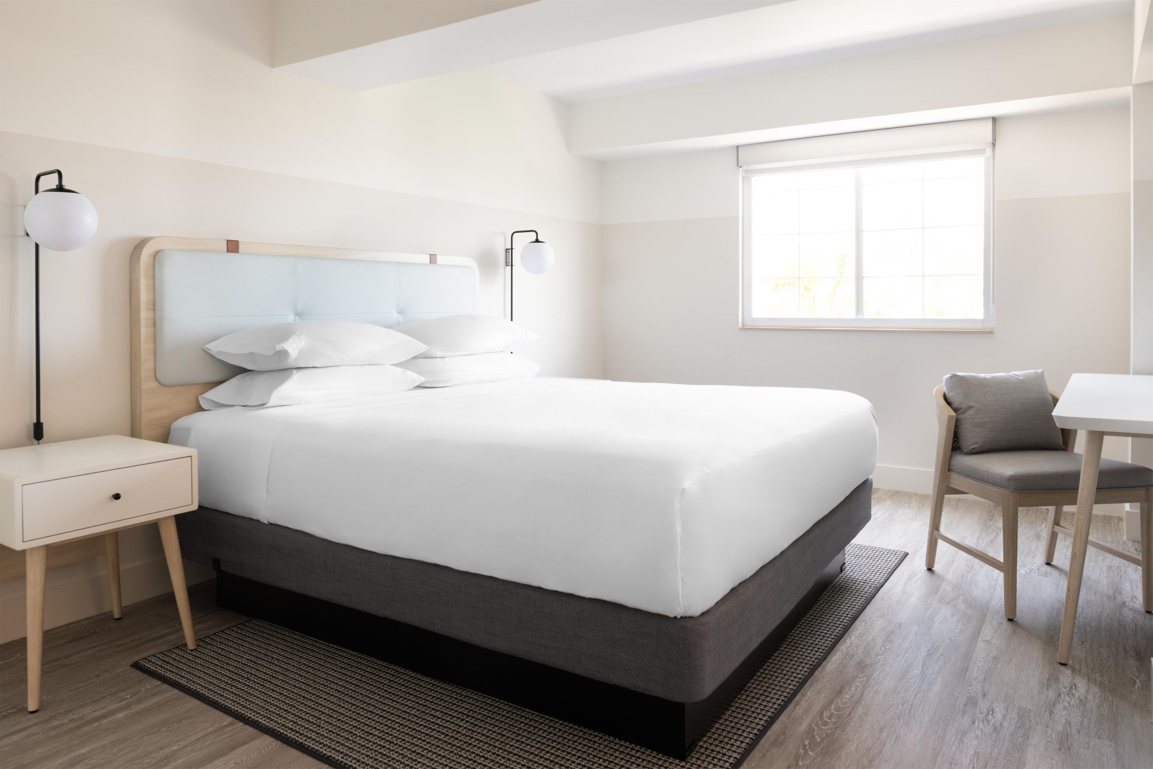 A modern hotel room with a large bed, bedside tables, a desk, and a chair.