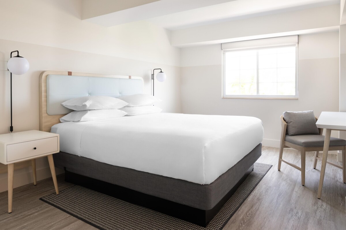 A modern hotel room with a large bed, bedside tables, a desk, and a chair.