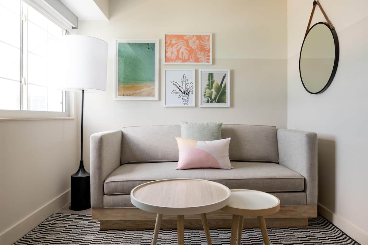 A modern living room with a grey sofa, two round wooden tables, a floor lamp, and three framed artworks on the wall.