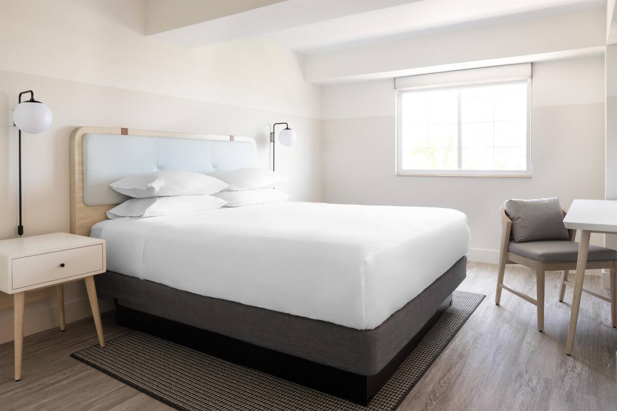 A modern hotel room with a large bed, bedside tables, a desk, and a chair.