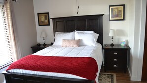 A neatly made bed with a red blanket, a dark headboard, two bedside tables with lamps, and a framed picture on the wall.