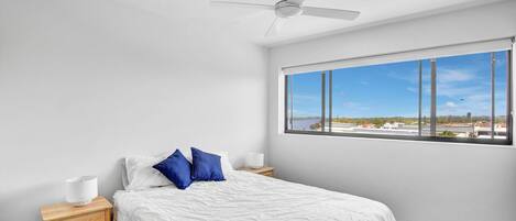 A bedroom with a bed, a nightstand, a ceiling fan, and a window with a city view.