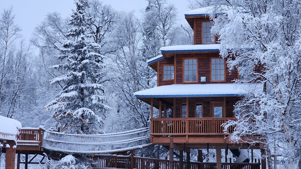 Eine mehrstöckige Holzhütte mit Balkon, umgeben von schneebedeckten Bäumen.