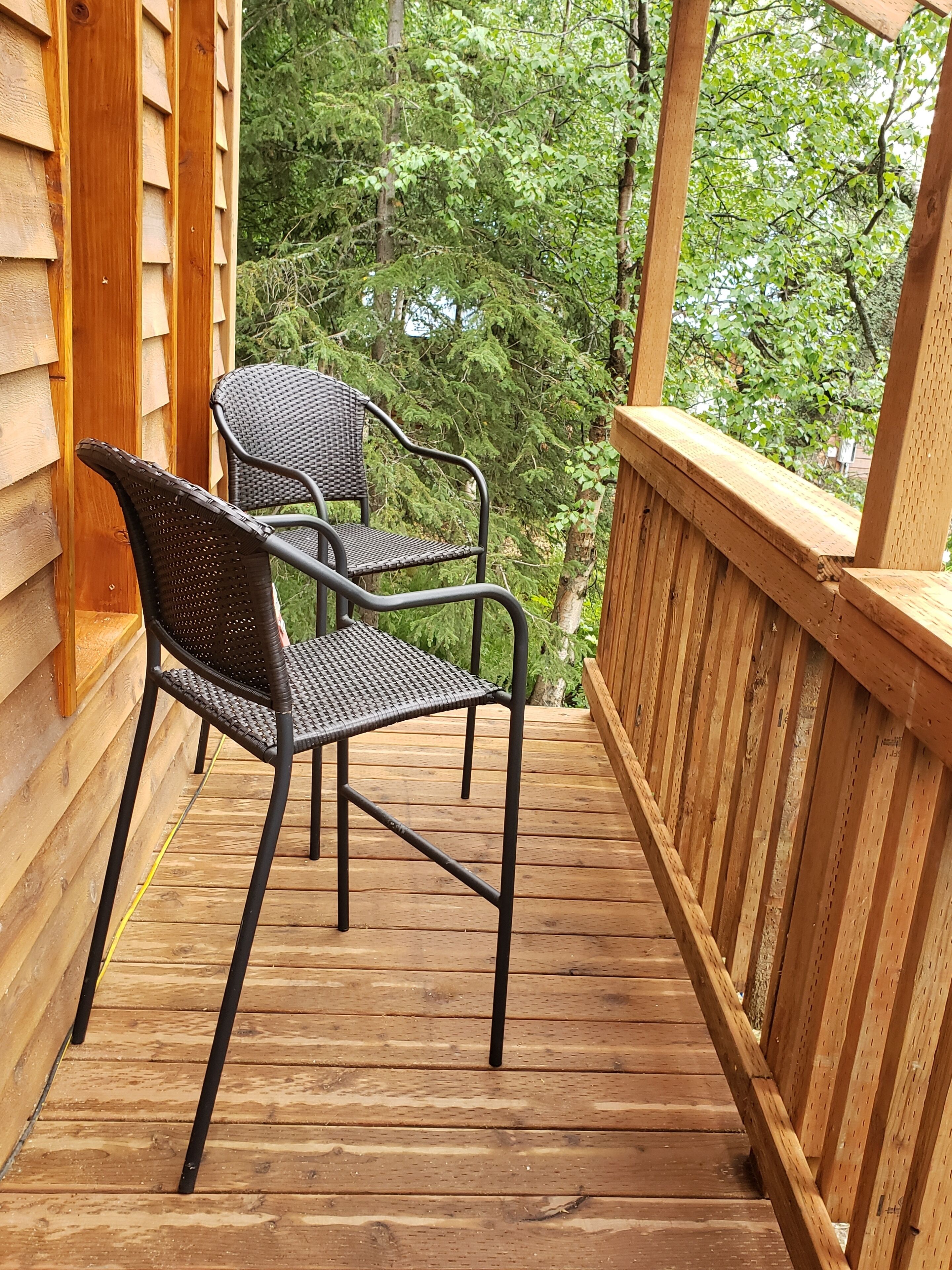 Une terrasse en bois avec deux chaises en osier et une rambarde en bois.