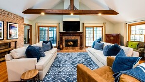 A spacious living room with a fireplace, two sofas, and a large window. - 2027 NOW OPEN! Harbert Home With Hot Tub & Close To Beach! (Harbert)