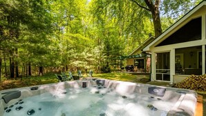 A hot tub in a forested backyard with a house and outdoor seating. - 2027 NOW OPEN! Harbert Home With Hot Tub & Close To Beach! (Harbert)