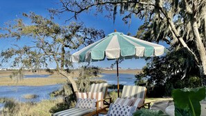 A patio with two striped lounge chairs, a green and white striped umbrella, and a view of a body of water and trees. - Water views & only 2 miles to downtown  (Charleston)
