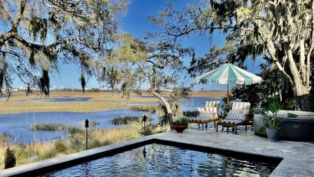 A swimming pool with a view of a water body and trees. There are lounge chairs and an umbrella. - Water views & only 2 miles to downtown  (Charleston)