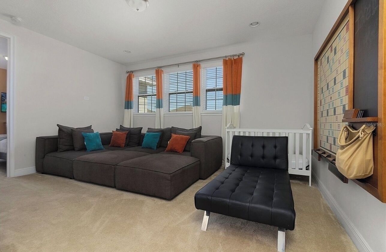 A living room with a sectional sofa, a black ottoman, and a white crib.