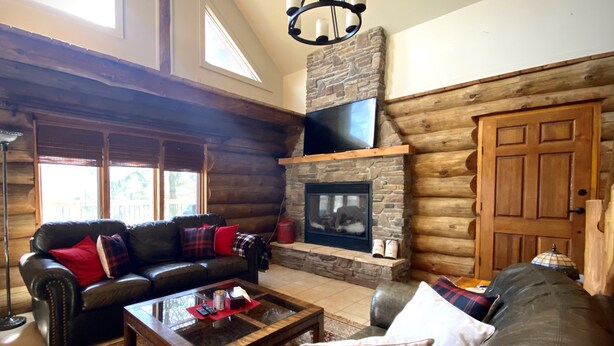 A log cabin interior with a stone fireplace, leather sofas, and a large window.
