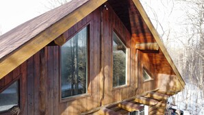 A wooden cabin with large windows and a staircase leading to the entrance.