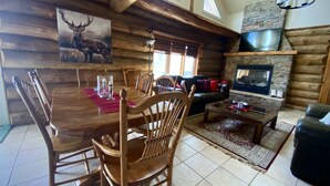 A log cabin interior with a dining area, a fireplace, and a cozy living room.
