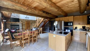 A spacious log cabin interior with a dining area, kitchen, and a staircase leading to a loft.