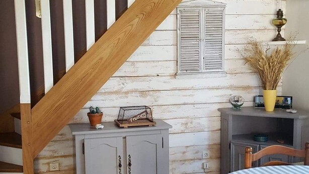 Una habitación rústica con una escalera de madera, una cama con ropa de cama a rayas, un mueble pequeño y un calentador fijado a la pared.