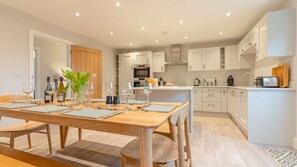 A modern kitchen with white cabinets, a dining table set for six, and a small island with a toaster. - Maple House - sleeps 9 guests  in 5 bedrooms (Ebrington)