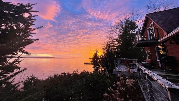 A waterfront property with a wooden deck, a covered porch, and a view of the sunset over the water. - Waterfront Escape at the Tip of Door County (Ellison Bay)
