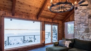 A cozy cabin interior with a wooden ceiling, large windows overlooking a snowy landscape, and a stone wall. - Waterfront Escape at the Tip of Door County (Ellison Bay)