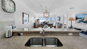 A modern kitchen with granite countertops, a double sink, and a dining area with a view of the sea.