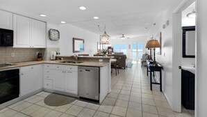 A spacious kitchen with white cabinetry, a built-in dishwasher, and a large island with a sink. There is a dining area with a view of the ocean.