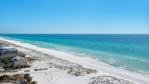 A beach view with a building on the left, clear blue water, and a sandy beach.