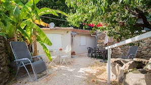 Eine Terrasse mit Steinmauern, einem weißen Zaun und Gartenmöbeln, darunter Stühle und ein Tisch.
