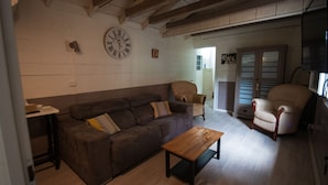 Ein Wohnzimmer mit braunem Sofa, einem Holztisch und zwei Sesseln. Eine Uhr ist an der Wand befestigt.