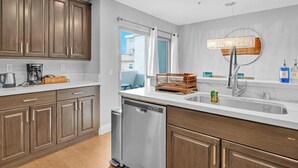 A modern kitchen with wooden cabinets, a dishwasher, a coffee maker, and a window with curtains.