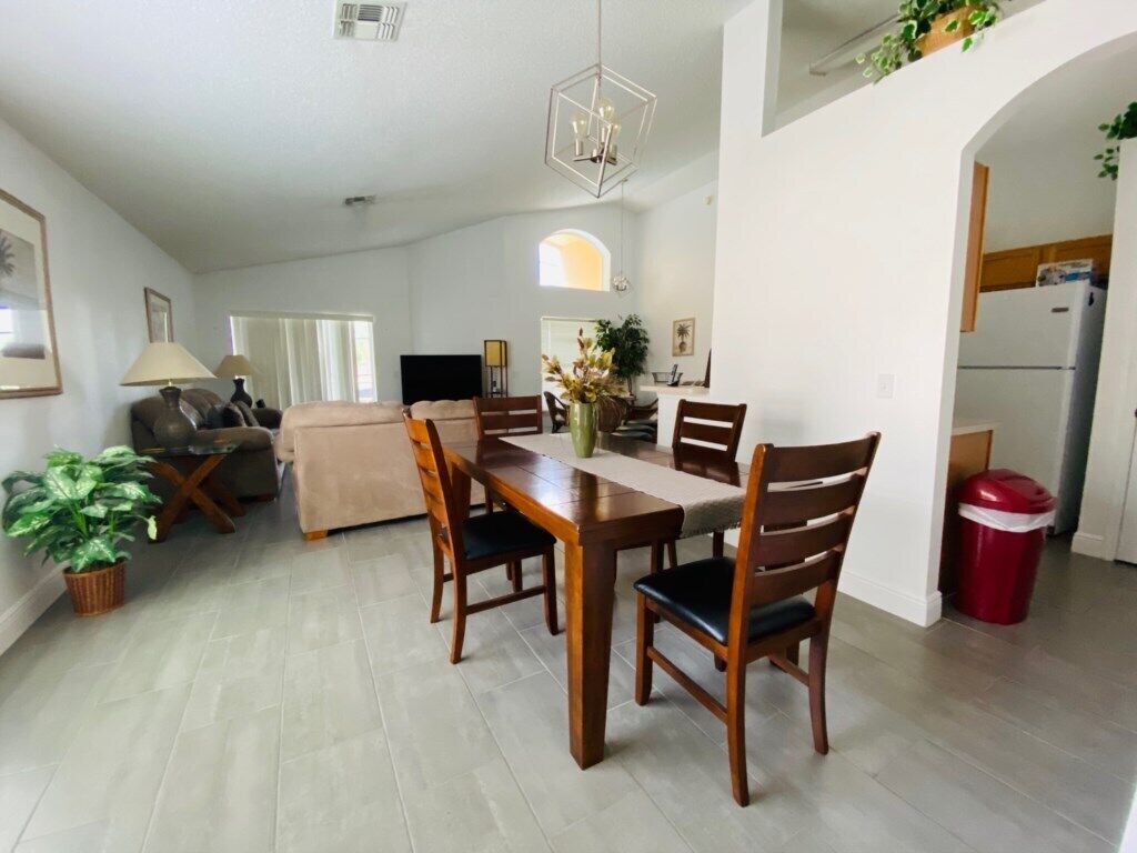Un grand espace de vie comprenant un coin repas avec une table, des chaises et un canapé. Il y a également une cuisine équipée d’un réfrigérateur et d’une poubelle.