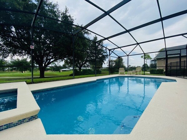 Una piscina con area coperta, circondata da alberi e un prato.