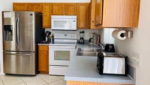 A modern kitchen with stainless steel appliances, wooden cabinets, and a granite countertop. - Golf Course Views - Heatable Pool -  Southern Dunes (Haines City)