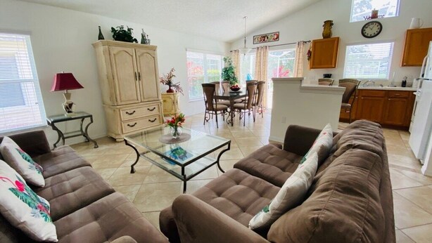 A living room with a brown sofa set, a glass coffee table, and a dining area with a table and chairs. - Golf Course Views - Private Pool - WiFi - Southern Dunes Golf & Contry Club (Haines City)
