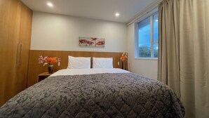 Un cuarto de hotel con una cama grande, una mesita de noche con un florero, un cuadro en la pared y una ventana con cortinas.