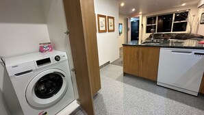 Zona de lavandería con lavadora Haier blanca, una puerta de madera, una cocina con lavavajillas blanco y una encimera.