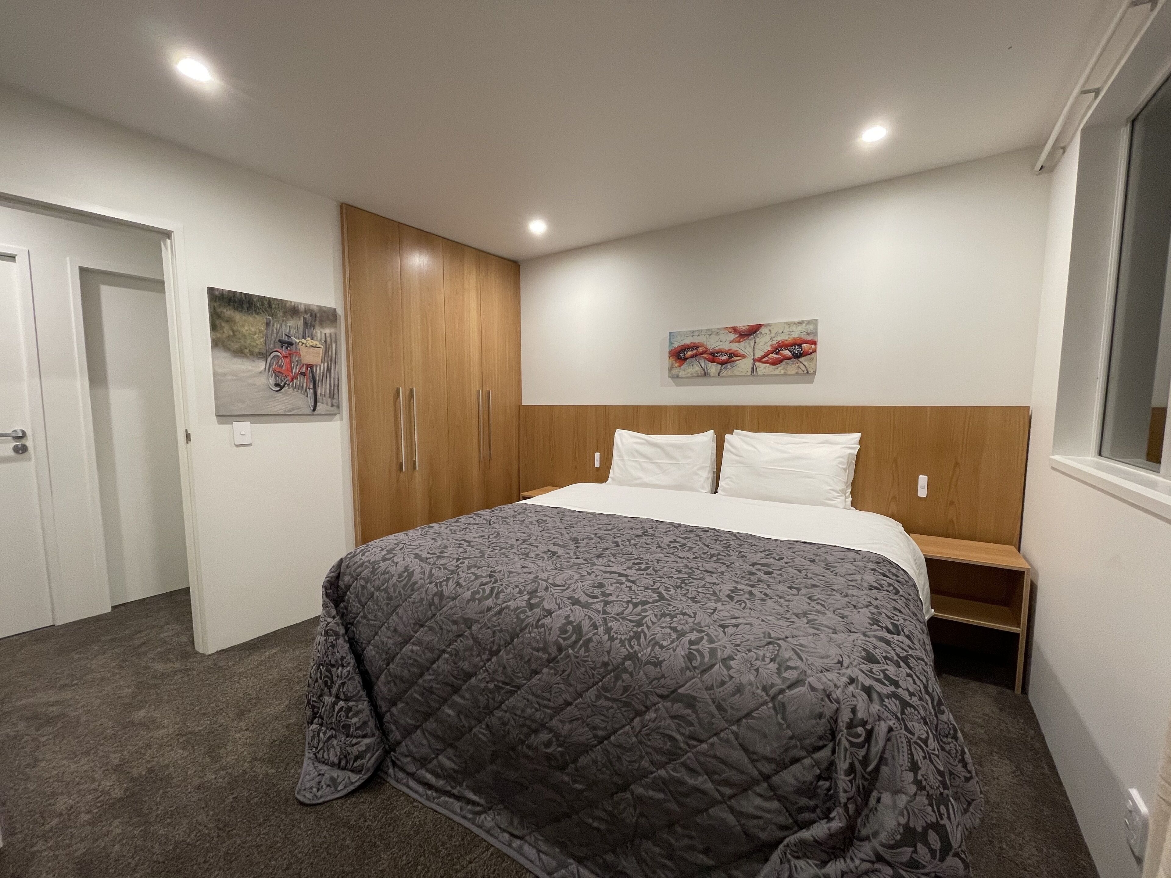 A bedroom with a bed, a wardrobe, a nightstand, and artwork on the walls.