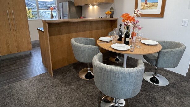 Una cocina moderna con armarios de madera, un comedor con sillas tapizadas en gris y una pequeña isla con un florero.