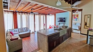 A modern living room with a sofa, a dining area with a kitchen island, and a TV mounted on the wall. - Luxury villas Playa Avellanas (Guanacaste)