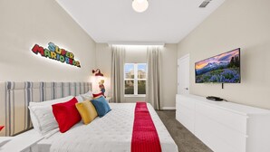 Une chambre d’hôtel avec un lit, une télévision, une fenêtre avec des rideaux et un mur orné d’une affiche de Super Mario Bros.