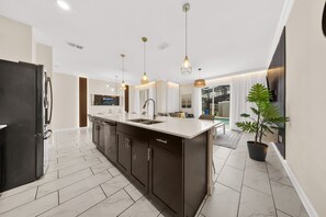Une cuisine moderne dotée d’un îlot central, de meubles de rangement aux couleurs sombres et d’un grand réfrigérateur.