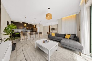 Un salon moderne avec un canapé gris, une table basse blanche et une cuisine en arrière-plan.
